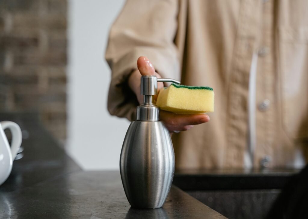 pexels photo 7641420 7641420 Close-up of a person using a metal soap dispenser with a cleaning sponge indoors.